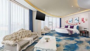 A hotel room with a large bed, a sofa, a coffee table, and a flat-screen TV.