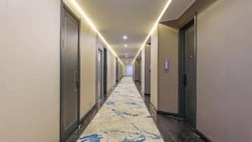 A hotel corridor with doors on both sides, a patterned carpet, and overhead lighting.