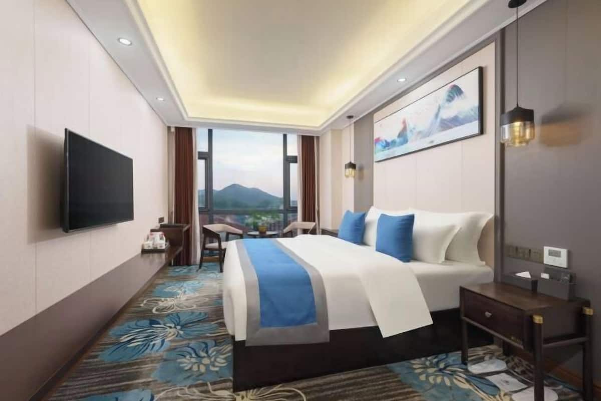 Una habitación de hotel con cama, televisor, escritorio y vistas a las montañas.