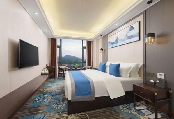 Quarto de hotel com cama, televisão, escrivaninha e janela com vista para as montanhas.