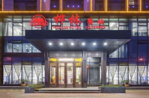 Entrada de un hotel con fachada de vidrio y un letrero que indica que es un hotel y servicio de catering.