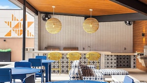 A modern outdoor seating area with blue tables and chairs, yellow woven light fixtures, and patterned cushions. - The Mercer (New Braunfels)