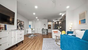 A modern living room with a blue sofa, white armchairs, and a dining area with a white table and chairs. - The Mercer (New Braunfels)