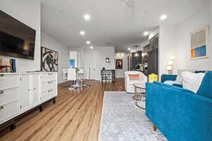 Uma sala de estar moderna com um sofá azul, poltronas brancas e uma área de jantar com uma mesa e cadeiras brancas.