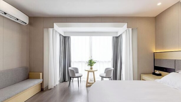 A modern hotel room with a large bed, a seating area, a small table with chairs, and a window with curtains. - Yizhou Hotel (Shanghai)