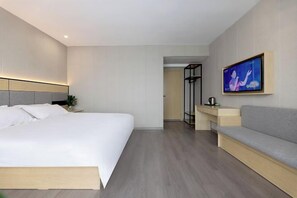 Quarto de hotel moderno com uma cama grande, um sofá, uma televisão e um closet espaçoso.