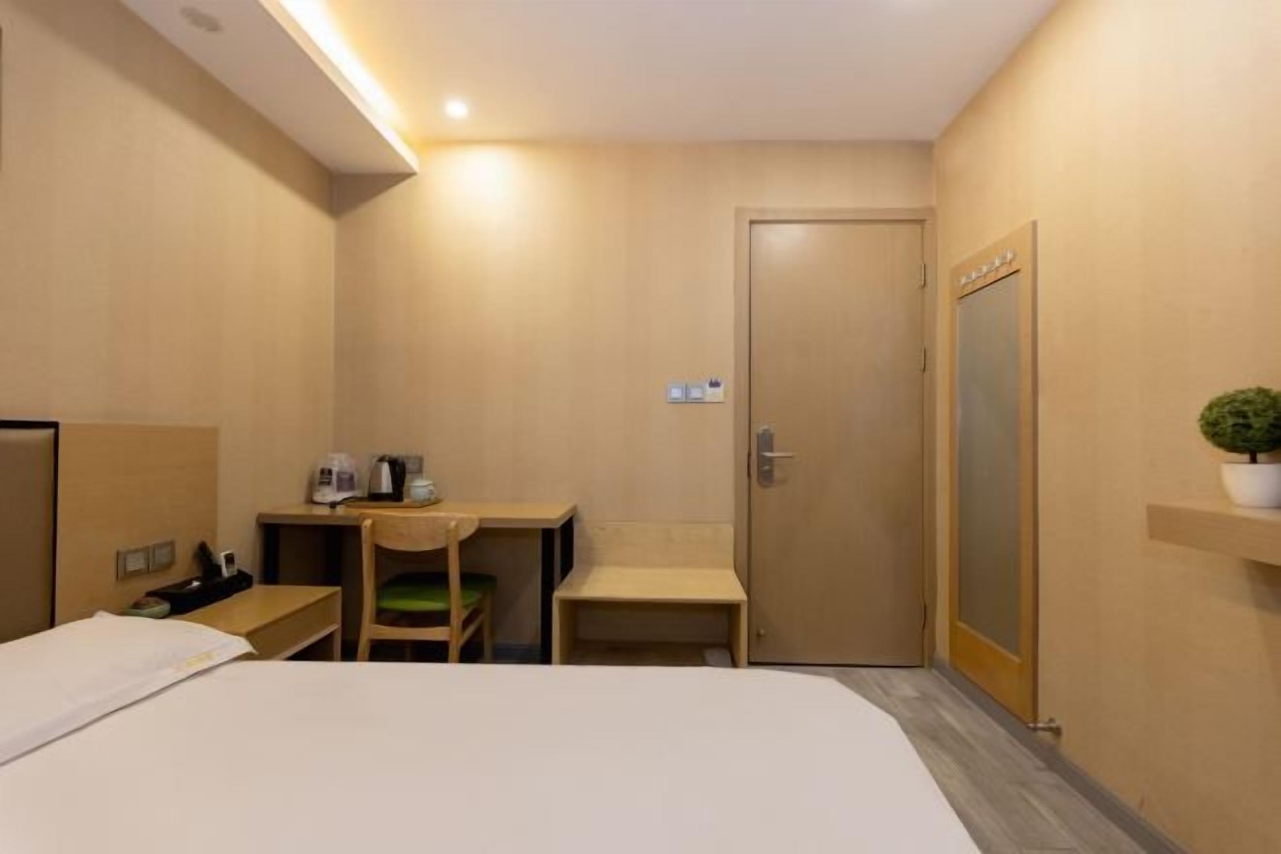 Een hotelkamer met een bed, een bureau, een stoel, een bijzettafeltje, een spiegel en een plant in pot.