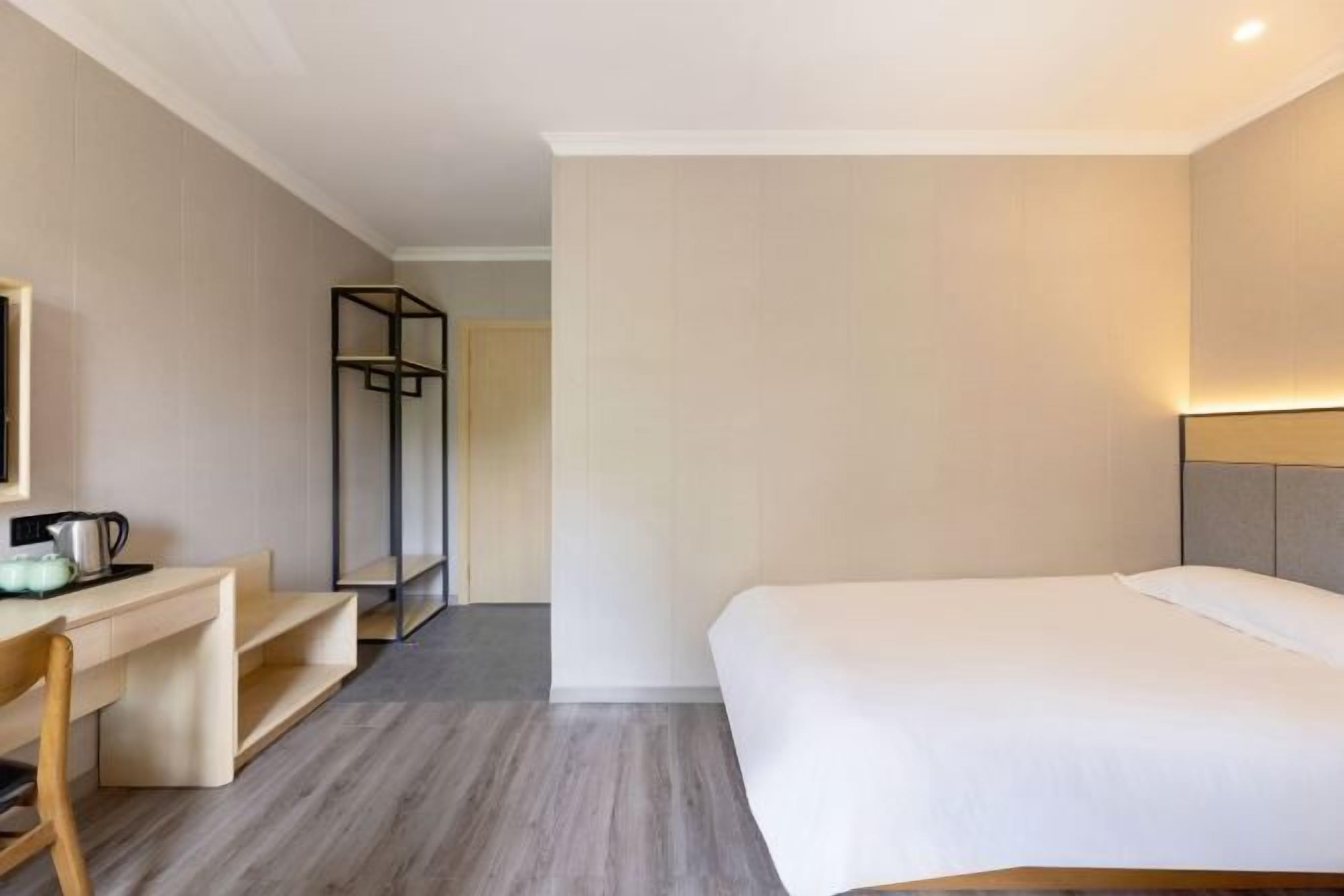 A hotel room with a bed, a desk with a chair, a small table with a kettle, and a wardrobe.