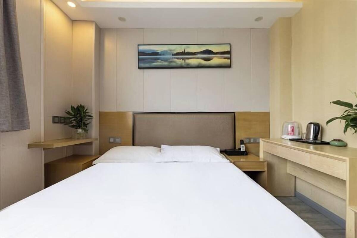 A hotel room with a bed, bedside table, nightstand, and a painting on the wall.