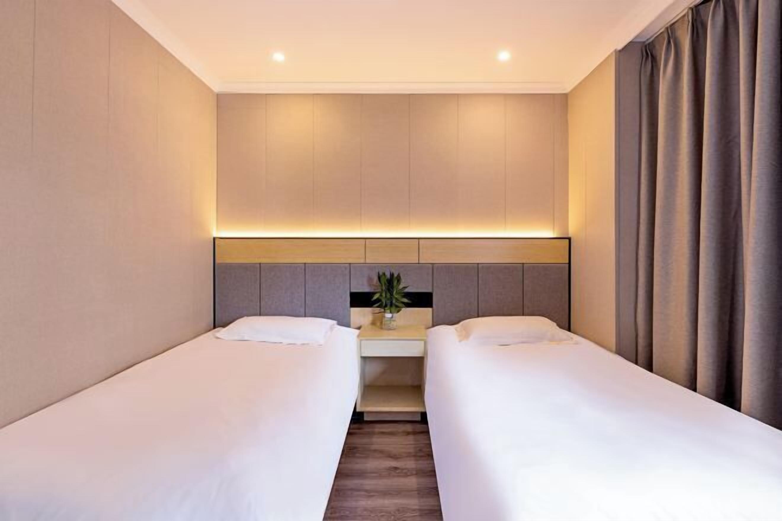 Et hotelværelse med to enkeltsenge, et natbord med lampe og en sengegavl med indbygget lys.