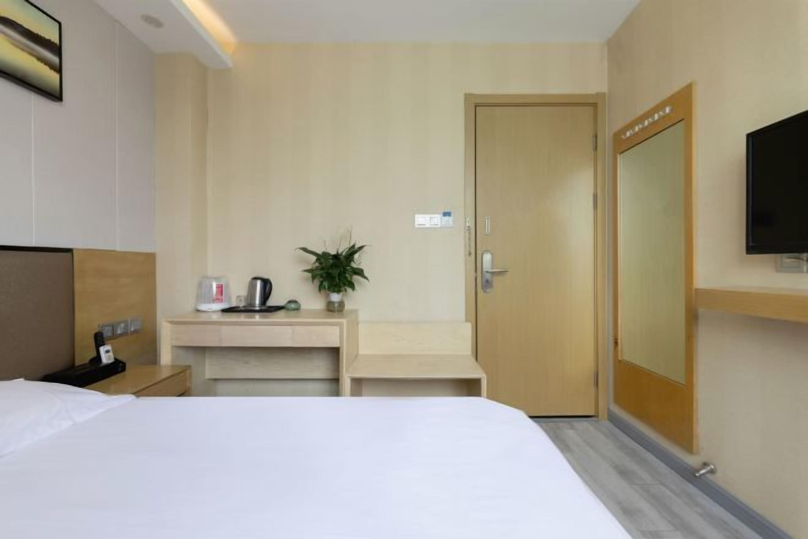 A hotel room with a bed, a desk with a plant, a coffee maker, and a TV mounted on the wall.