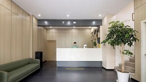 A reception area with a reception desk, a green sofa, a potted plant, and a speaker. - Yizhou Hotel (Shanghai)
