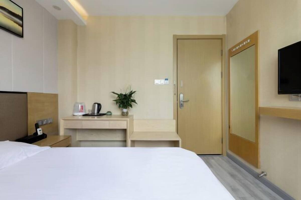 A hotel room with a bed, a desk with a plant, a coffee maker, a TV, and a door.