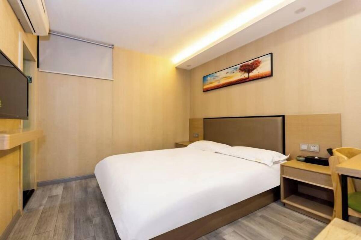 A hotel room with a bed, bedside table, chair, and a painting on the wall.