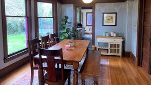 A dining room with a wooden table and chairs, large windows, a chandelier, and a view of the garden. - 5-min walk to Downtown Olympia and Capital Lake, 4br, sleeps 13 (Olympia)