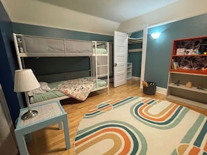 Un dormitorio con literas, un escritorio, una lámpara, una alfombra y una estantería con juguetes.