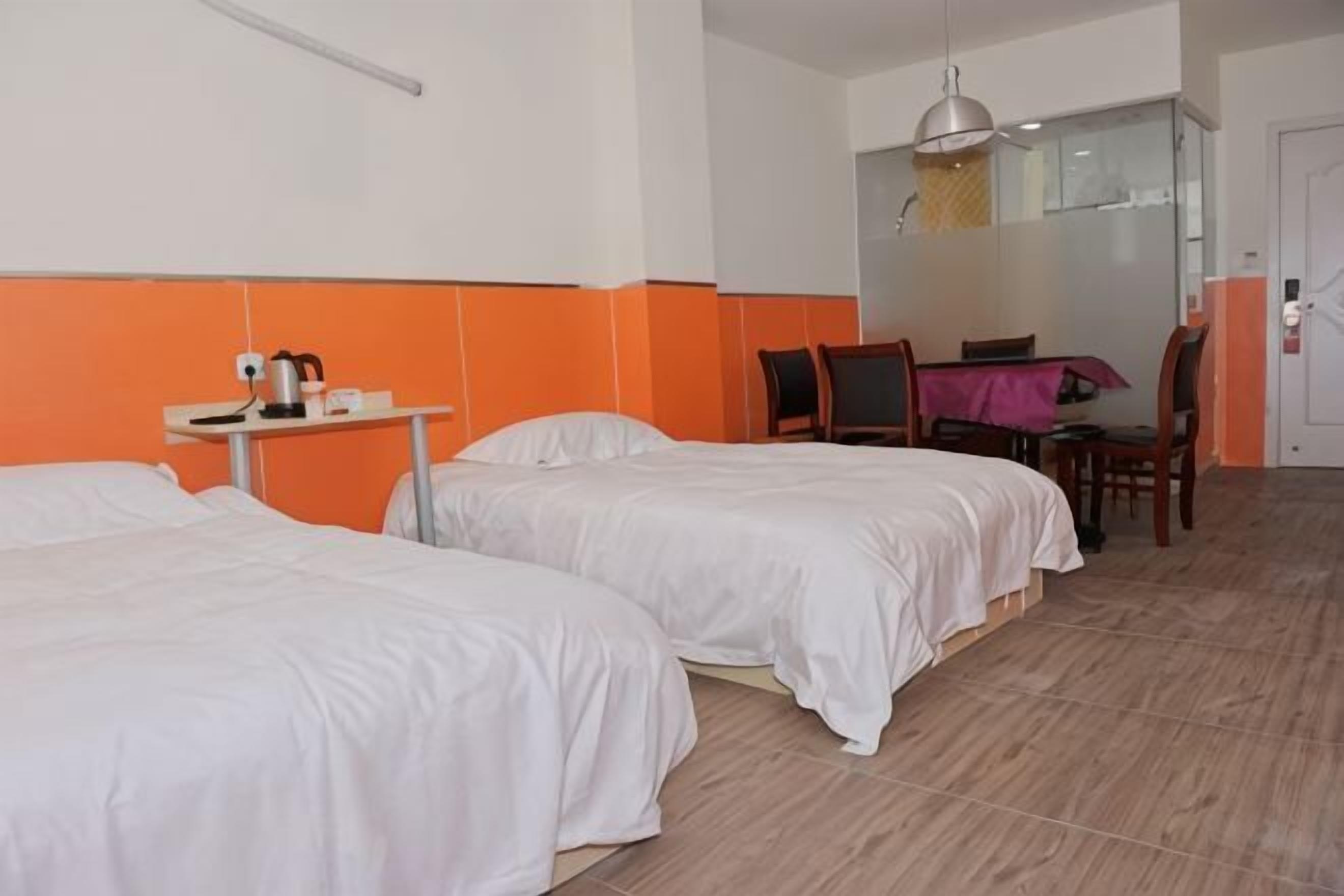 A hotel room with two beds, a small table with a kettle, a chair, and a dining table with chairs.