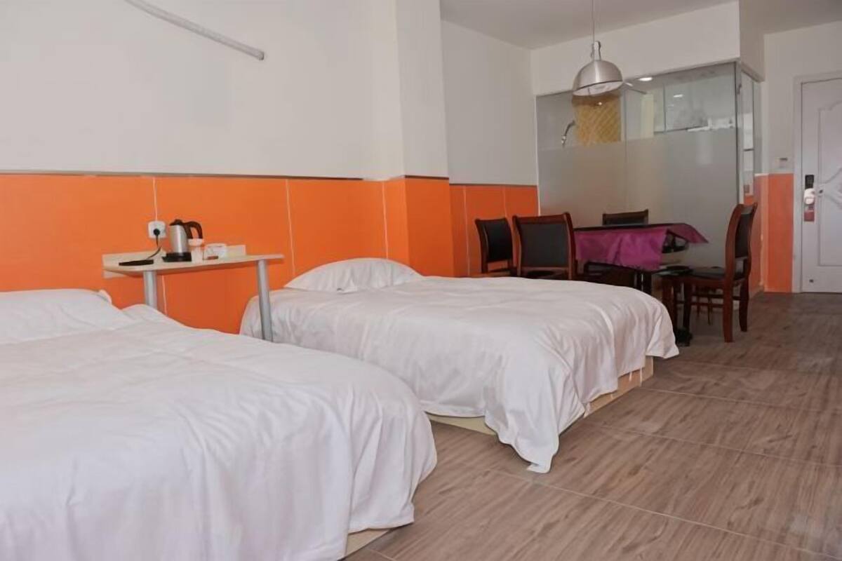 A hotel room with two beds, a small table with a kettle, a chair, and a dining table with chairs.