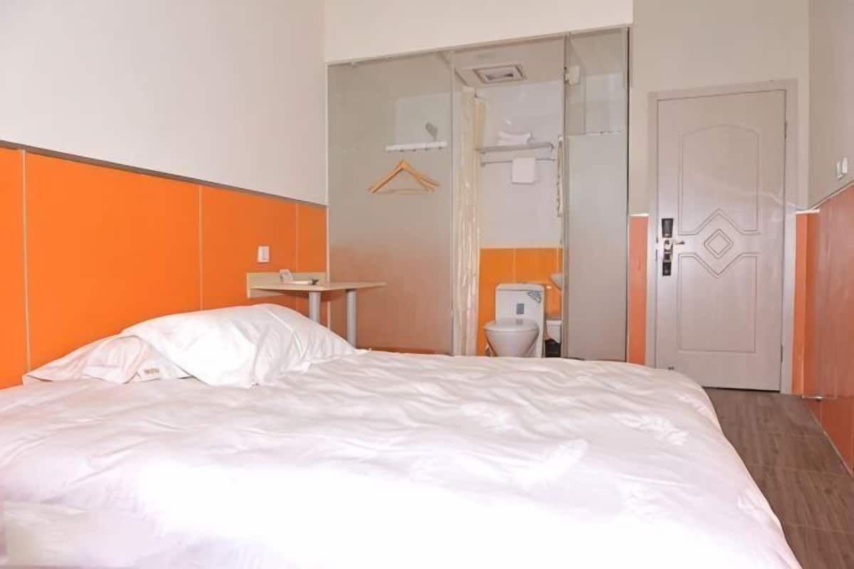 A hotel room with a bed, a small table, a toilet, and a door.
