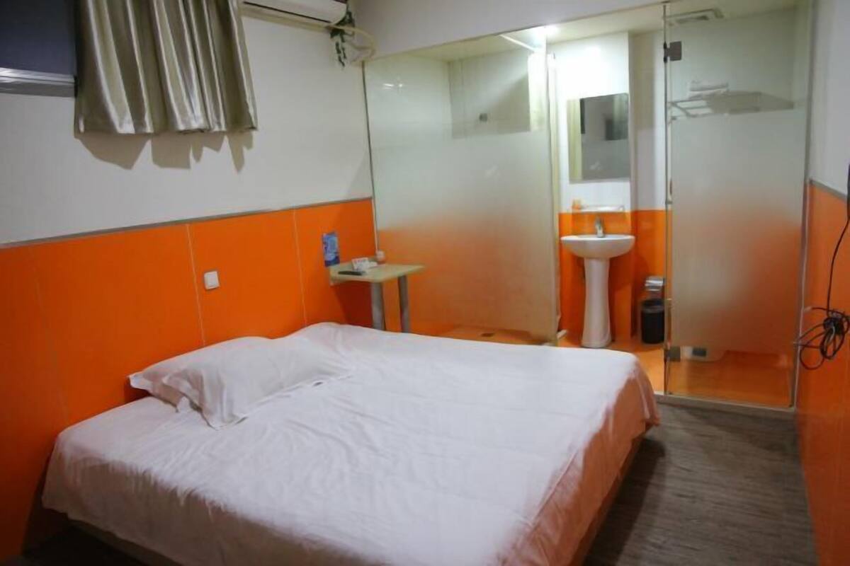A hotel room with a bed, a small table with a lamp, a bathroom with a sink, and a mirror.