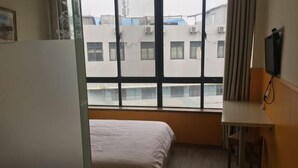 A hotel room with a bed, a desk, a chair, a TV, and a window with a view of buildings. - Chaolv 98 Hostel (Shanghai University) (Shanghai)