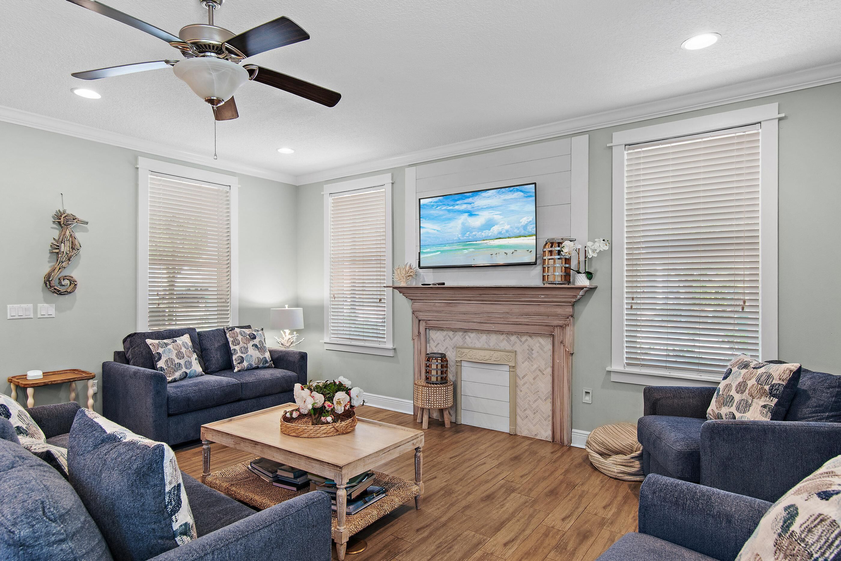 A living room with a fireplace, a ceiling fan, and a television on the wall.