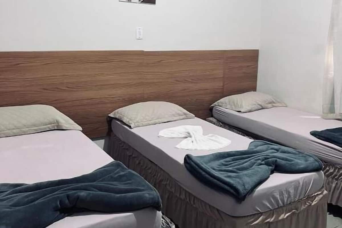A room with three single beds, each with a pillow and a blanket. There is a wooden headboard on the wall, and a small picture frame above the beds.