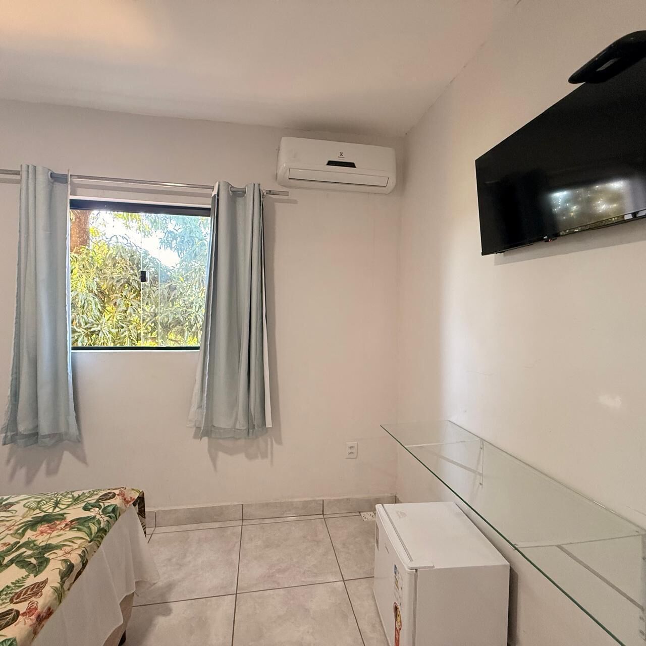 A room with a bed, an air conditioning unit, a television, and a small white appliance.