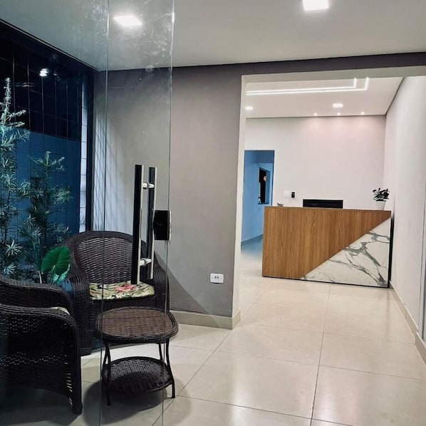 A modern reception area with a wooden reception desk, a glass partition, and wicker furniture.