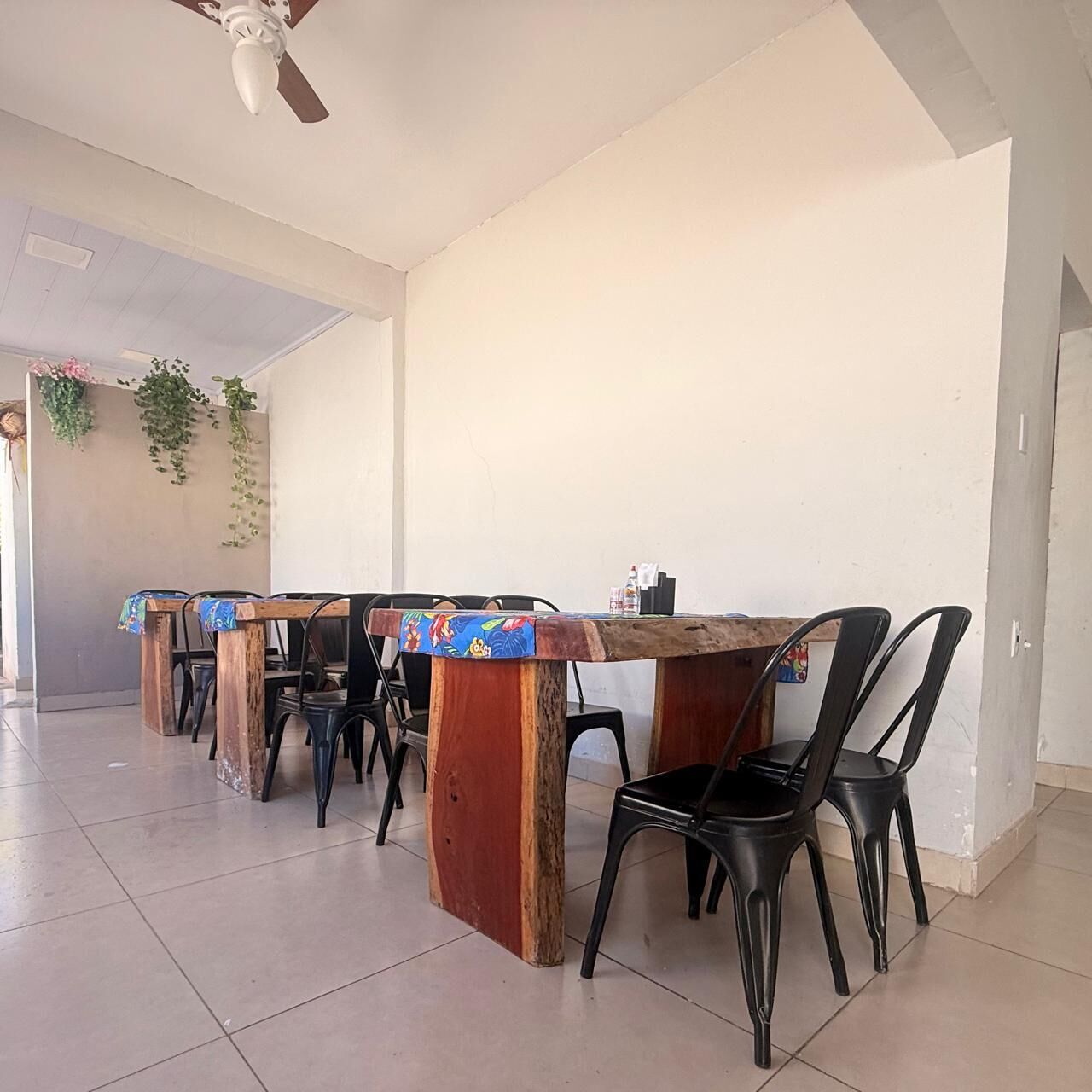 A dining area with a wooden table and black chairs, a ceiling fan, and hanging plants.