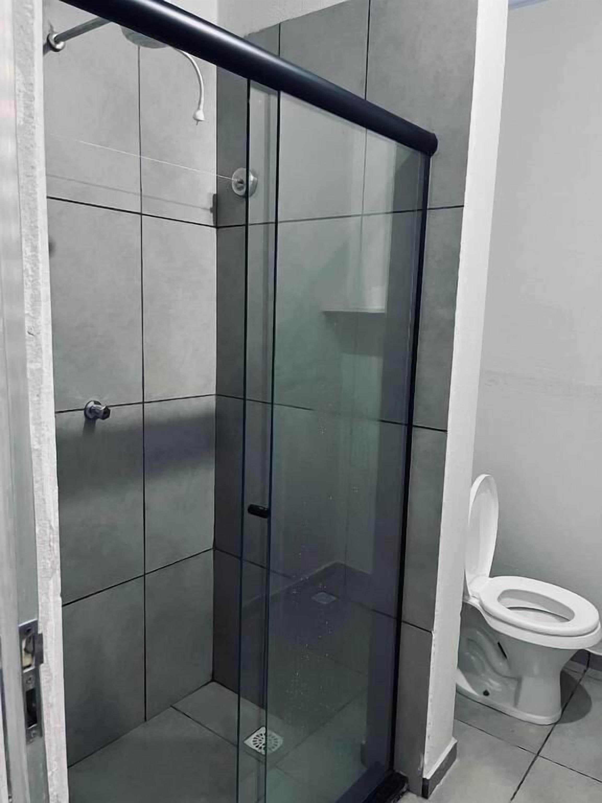 Un baño moderno con ducha envuelta en vidrio, un inodoro y un pasamanos de metal.