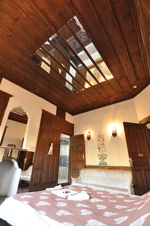 A bedroom with a sloped ceiling, a large bed with a floral bedspread, a wooden wardrobe, and a wall-mounted light fixture. - HAN SAFRANBOLU KONAKLAMA TESİSİ (Safranbolu)