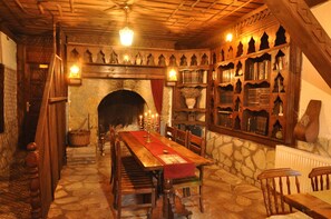 Um quarto tradicional com lareira de pedra, estantes de madeira e uma longa mesa de madeira com cadeiras.