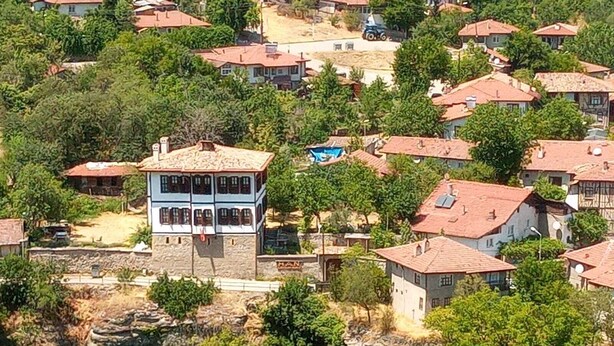 A residential area with houses featuring red-tiled roofs and a prominent two-story building with a stone facade.