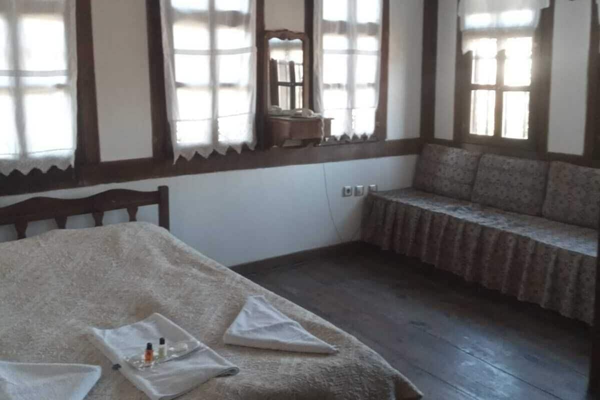Quarto com cama, um banco e janelas amplas.