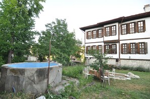 A two-story building with a white facade and brown window shutters, a concrete pool, and a garden with chairs and tables. - HAN SAFRANBOLU KONAKLAMA TESİSİ (Safranbolu)