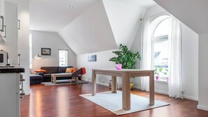 A modern living room with a wooden floor, a dining table, a sofa, and a large window with curtains. - Penthouse by Brosundet, Free Parking Space (Ålesund)