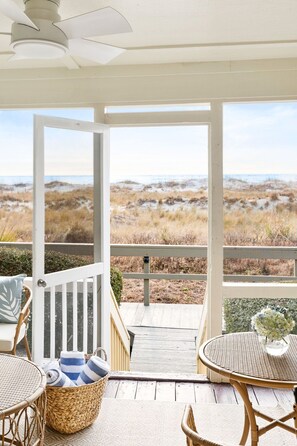 A covered outdoor area with wicker furniture, a view of the beach, and a wooden deck leading to the beach. - The Blue Palm • Oceanfront • Mariner's Walk 2B • Wild Dunes • Isle of Palms, SC (Isle of Palms)