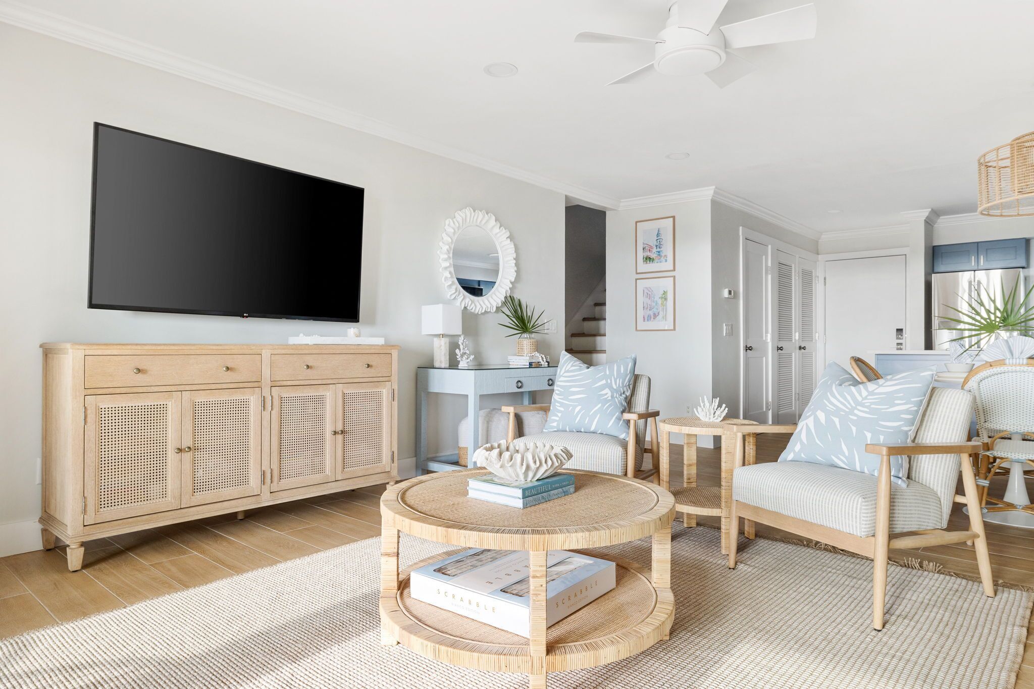 Een woonkamer met een flatscreen televisie, een ronde salontafel, rieten stoelen en een lichtkleurige bank.