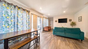 A living room with a wooden dining table, benches, a teal sofa, and a television mounted on the wall. - 5BedR, Sleeps 16, Big Yard, Game Room, Pet OK, CVNP (Cuyahoga Falls)