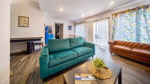 A modern living room with a teal sofa, a brown leather sofa, a coffee table with a magazine, and a large window with curtains. - 5BedR, Sleeps 16, Big Yard, Game Room, Pet OK, CVNP (Cuyahoga Falls)