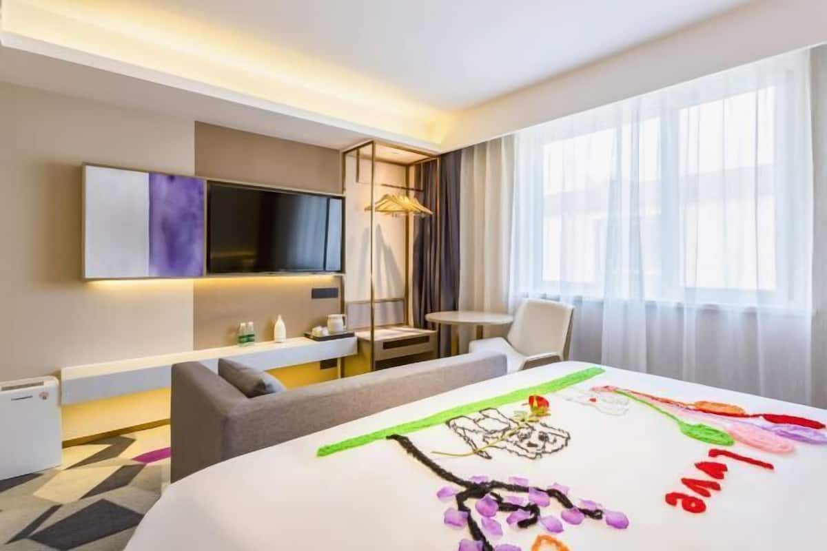 A hotel room with a bed, a TV, a desk, a chair, and a window with curtains.