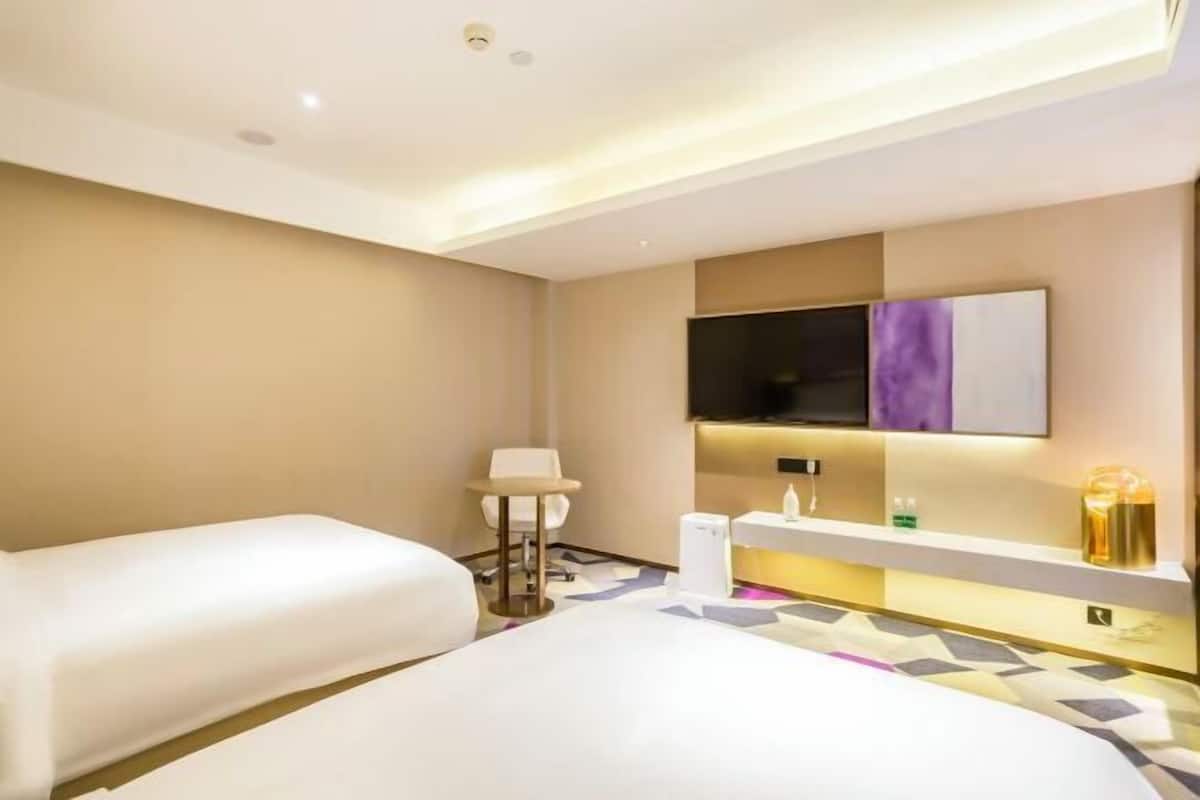 A hotel room with two beds, a TV, a desk, and a bathroom.