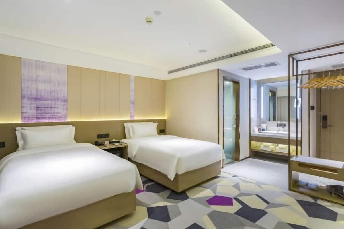 A hotel room with two beds, a bathroom with a mirror, and a geometric patterned floor.