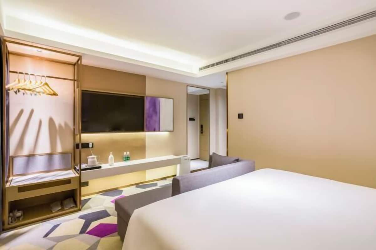 A modern hotel room with a large bed, a seating area, a vanity with toiletries, and a wardrobe with hanging clothes.