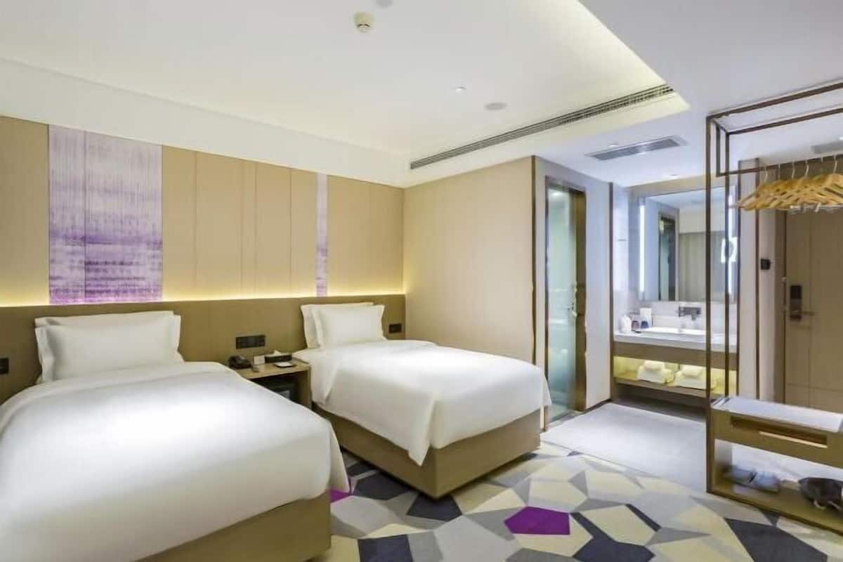 A hotel room with two beds, a large mirror, a bathroom with a vanity, and a geometric patterned floor.