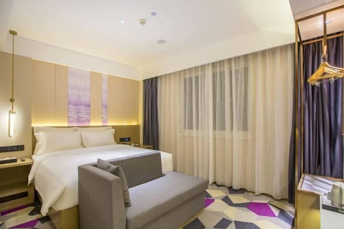 A hotel room with a bed, a sofa, a desk, and a large window with curtains.