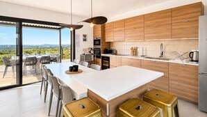 A modern kitchen with a large island, wooden cabinets, and a view of the countryside.