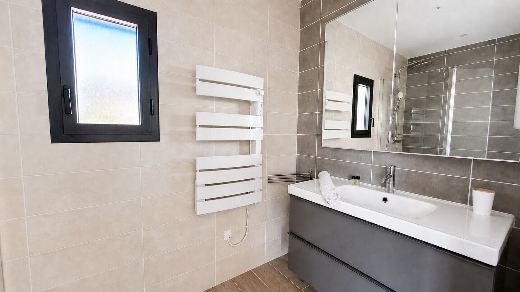 A modern bathroom with a large mirror, a white sink, and a towel rack.
