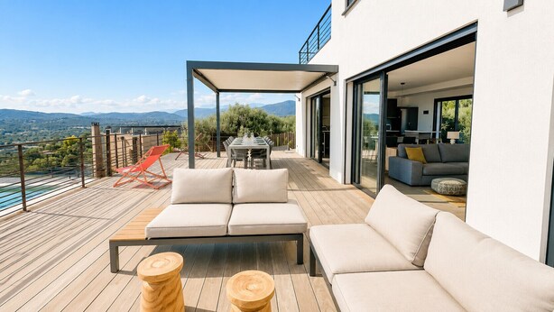 A modern outdoor living area with a sofa, chairs, and a table, overlooking a scenic landscape.